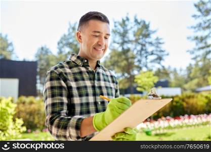 gardening and people concept - happy smiling middle-aged man in gloves writing to clipboard at summer garden. happy man with clipboard at summer garden