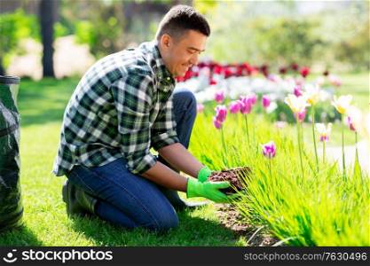 gardening and people concept - happy smiling middle-aged man taking care of flowers at summer garden. middle-aged man taking care of flowers at garden