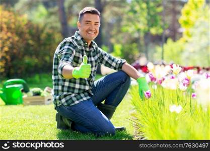 gardening and people concept - happy smiling middle-aged man taking care of flowers and showing thumbs up at summer garden. happy man with flowers showing thumbs up at garden