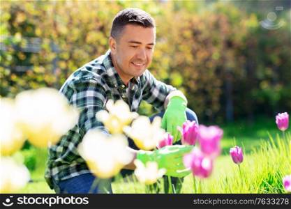 gardening and people concept - happy smiling middle-aged man taking care of flowers at summer garden. happy man taking care of flowers at garden