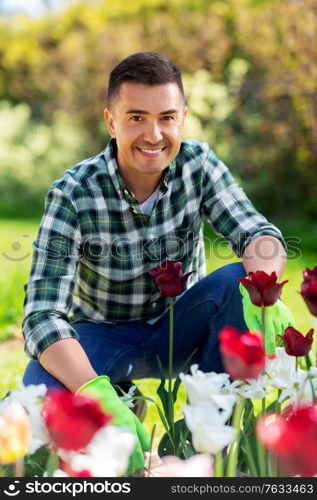 gardening and people concept - happy smiling middle-aged man taking care of flowers at summer garden. middle-aged man taking care of flowers at garden