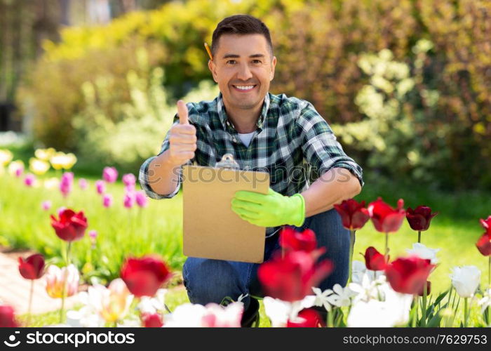 gardening and people concept - happy smiling middle-aged man with clipboard and taking care of flowers and showing thumbs up at summer garden. man with clipboard showing thumbs up garden