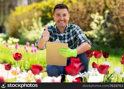 gardening and people concept - happy smiling middle-aged man with clipboard and taking care of flowers and showing thumbs up at summer garden. man with clipboard showing thumbs up garden