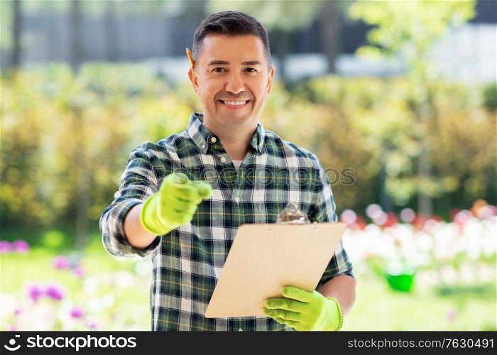 gardening and people concept - happy smiling middle-aged man with clipboard pointing finger to camera at summer garden. happy smiling man with clipboard at summer garden