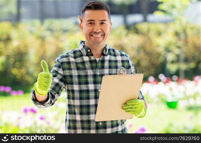 gardening and people concept - happy smiling middle-aged man with clipboard showing thumbs up at summer garden. man with clipboard showing thumbs up at garden