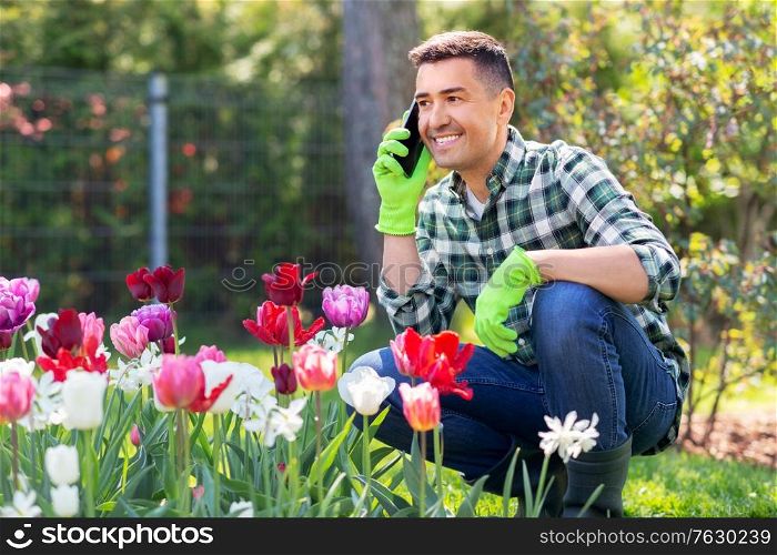 gardening and people concept - happy smiling middle-aged man with flowers calling on smartphone at summer garden. man with flowers calling on smartphone at garden