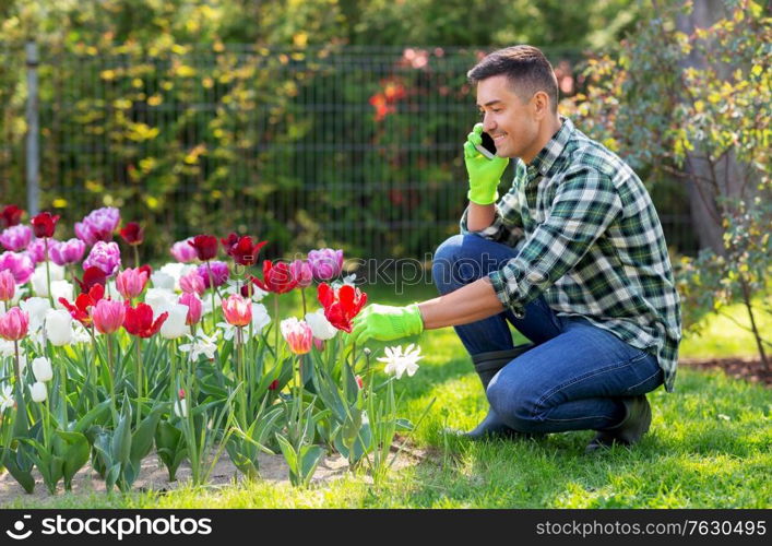 gardening and people concept - happy smiling middle-aged man with flowers calling on smartphone at summer garden. man with flowers calling on smartphone at garden