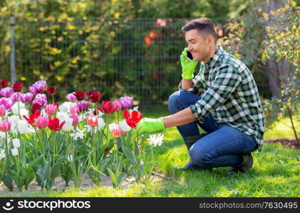 gardening and people concept - happy smiling middle-aged man with flowers calling on smartphone at summer garden. man with flowers calling on smartphone at garden