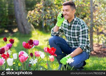 gardening and people concept - happy smiling middle-aged man with flowers calling on smartphone at summer garden. man with flowers calling on smartphone at garden