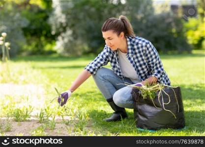 gardening and people concept - happy smiling woman with bag weeding flowerbed at summer garden. woman weeding flowerbed at summer garden