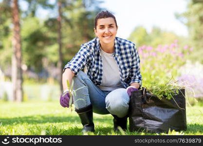 gardening and people concept - happy smiling woman with bag weeding flowerbed at summer garden. woman weeding flowerbed at summer garden