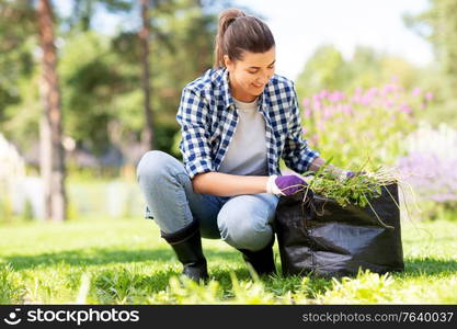 gardening and people concept - happy smiling woman with bag weeding flowerbed at summer garden. woman weeding flowerbed at summer garden