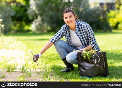 gardening and people concept - happy smiling woman with bag weeding flowerbed at summer garden. woman weeding flowerbed at summer garden