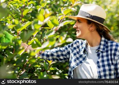 gardening and people concept - happy smiling young woman in straw hat working at summer garden. woman in hat working at summer garden