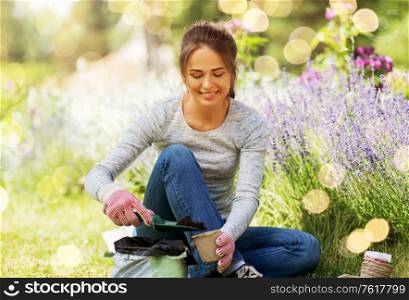 gardening and people concept - happy young woman filling pots with soil at summer garden over festive lights background. woman filling pots with soil at summer garden