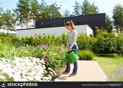gardening and people concept - happy young woman or gardener watering flowers at summer garden. young woman watering flowers at garden