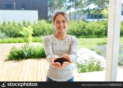 gardening and people concept - happy young woman or gardener with handful of soil at summer garden. young woman with handful of soil at summer garden