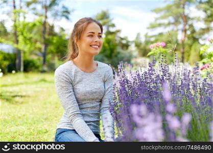 gardening and people concept - happy young woman sitting near lavender flowers on summer garden bed. young woman and lavender flowers at summer garden