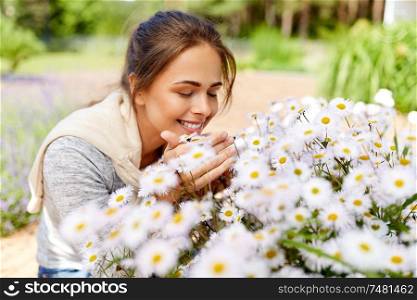 gardening and people concept - happy young woman smelling chamomile flowers at summer garden. happy woman smelling chamomile flowers in garden