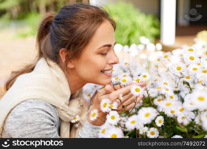 gardening and people concept - happy young woman smelling chamomile flowers at summer garden. happy woman smelling chamomile flowers in garden