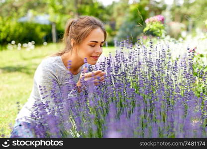 gardening and people concept - happy young woman smelling lavender flowers at summer garden. young woman smelling lavender flowers in garden