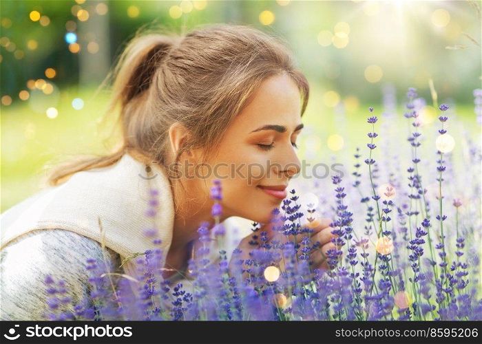 gardening and people concept - happy young woman smelling lavender flowers at summer garden. young woman smelling lavender flowers in garden