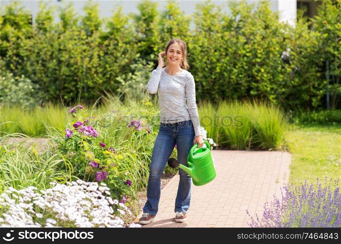 gardening and people concept - happy young woman with watering can and flowers at summer garden. young woman watering flowers at garden