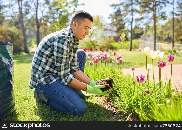 gardening and people concept - man pouring soil to flowers at summer garden. man pouring soil to flowers at summer garden