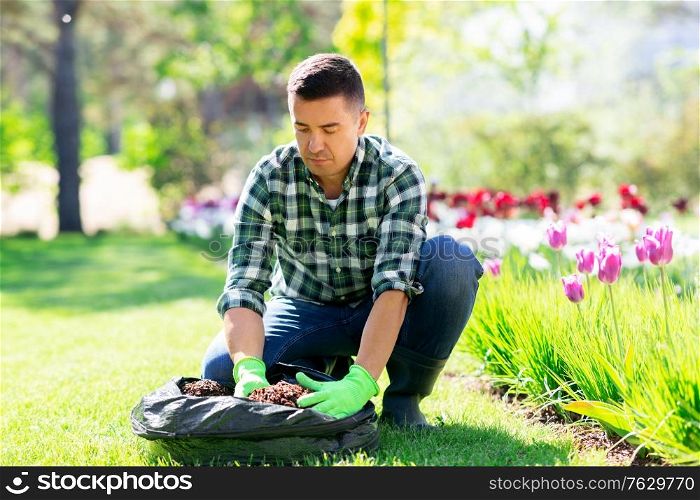 gardening and people concept - middle-aged man with soil in bag and flowers working at summer garden. man with soil in bag and flowers working at garden