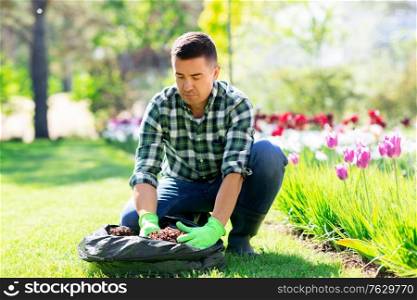 gardening and people concept - middle-aged man with soil in bag and flowers working at summer garden. man with soil in bag and flowers working at garden