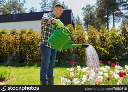 gardening and people concept - middle-aged man with watering can pouring water to flower bed at garden. middle-aged man watering flowers at garden