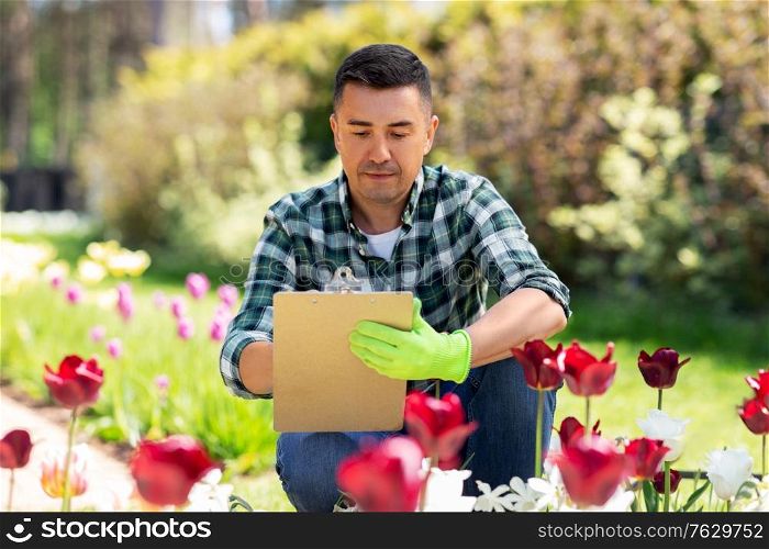 gardening and people concept - middle-aged man writing to clipboard and taking care of flowers at summer garden. man with clipboard and flowers at summer garden