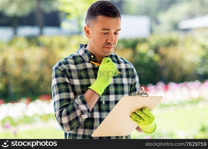 gardening and people concept - middle-aged man writing to clipboard at summer garden. man with clipboard at summer garden