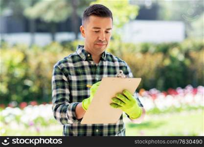 gardening and people concept - middle-aged man writing to clipboard at summer garden. man with clipboard at summer garden