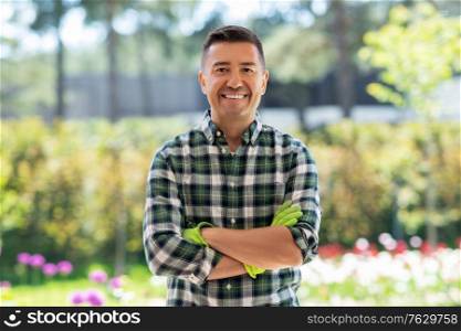 gardening and people concept - portrait of happy smiling middle-aged man with crossed arms in gloves at summer garden. happy smiling middle-aged man in gloves at garden
