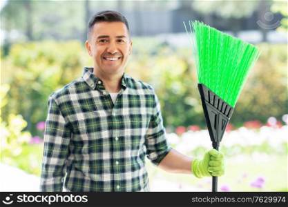 gardening and people concept - portrait of happy smiling middle-aged man with broom at summer garden. happy middle-aged man with broom at garden