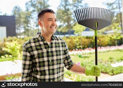 gardening and people concept - portrait of happy smiling middle-aged man with fan leaf rake in gloves at summer garden. happy middle-aged man with leaf rake at garden