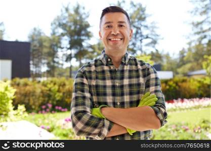 gardening and people concept - portrait of happy smiling middle-aged man with crossed arms in gloves at summer garden. happy smiling middle-aged man in gloves at garden