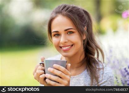 gardening and people concept - portrait of young woman drinking tea or coffee at summer garden. woman drinking tea or coffee at summer garden