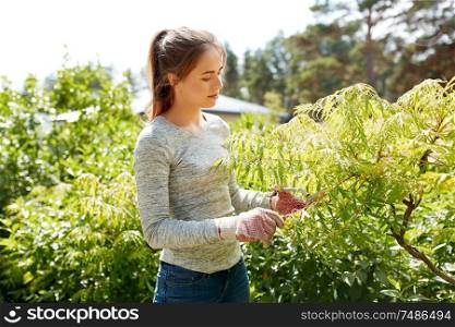 gardening and people concept - young woman or gardener with pruner taking care of bushes at summer garden. woman with pruner cutting bushes at summer garden