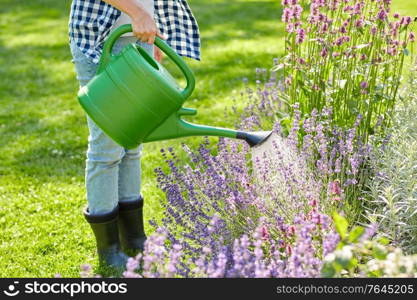 gardening and people concept - young woman with watering can pouring water to flowers at garden. young woman watering flowers at garden