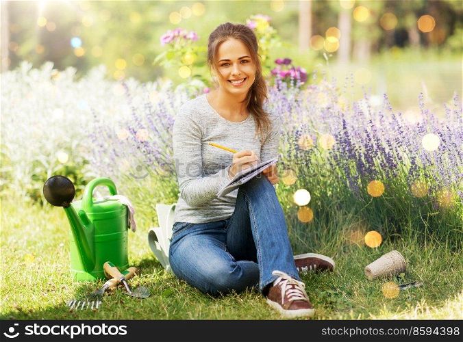 gardening and people concept - young woman writing to notebook at summer garden. young woman writing to notebook at summer garden
