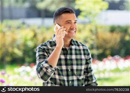 gardening, communication and people concept - happy smiling middle-aged man calling on smartphone at summer garden. happy man calling on smartphone at summer garden