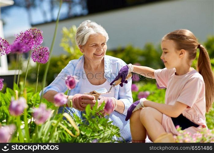 gardening, family and people concept - happy grandmother and granddaughter planting flowers at summer garden. grandmother and girl planting flowers at garden. grandmother and girl planting flowers at garden