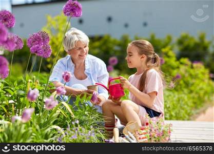 gardening, family and people concept - happy grandmother and granddaughter planting flowers at summer garden. grandmother and girl planting flowers at garden