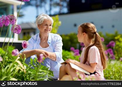 gardening, family and people concept - happy grandmother and granddaughter with notebook and flowers at summer garden. grandmother and granddaughter at summer garden