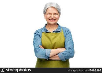 gardening, farming and old people concept - portrait of smiling senior woman in green garden with apron crossed arms over white background. portrait of smiling senior woman in garden apron