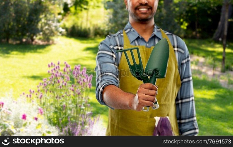 gardening, farming and people concept - close up of happy smiling indian male gardener or farmer in apron with garden tools over summer background. indian gardener or farmer with garden tools