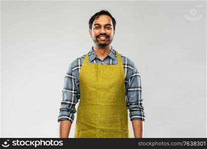 gardening, farming and people concept - happy smiling indian male gardener or farmer in apron over grey background. happy indian male gardener or farmer in apron