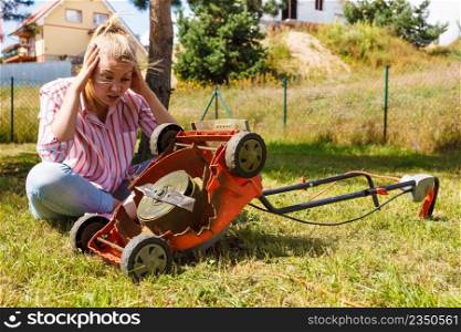Gardening. Female person gardener mowing green lawn with lawnmower, having problem with broken mower. Person having problem with land mower